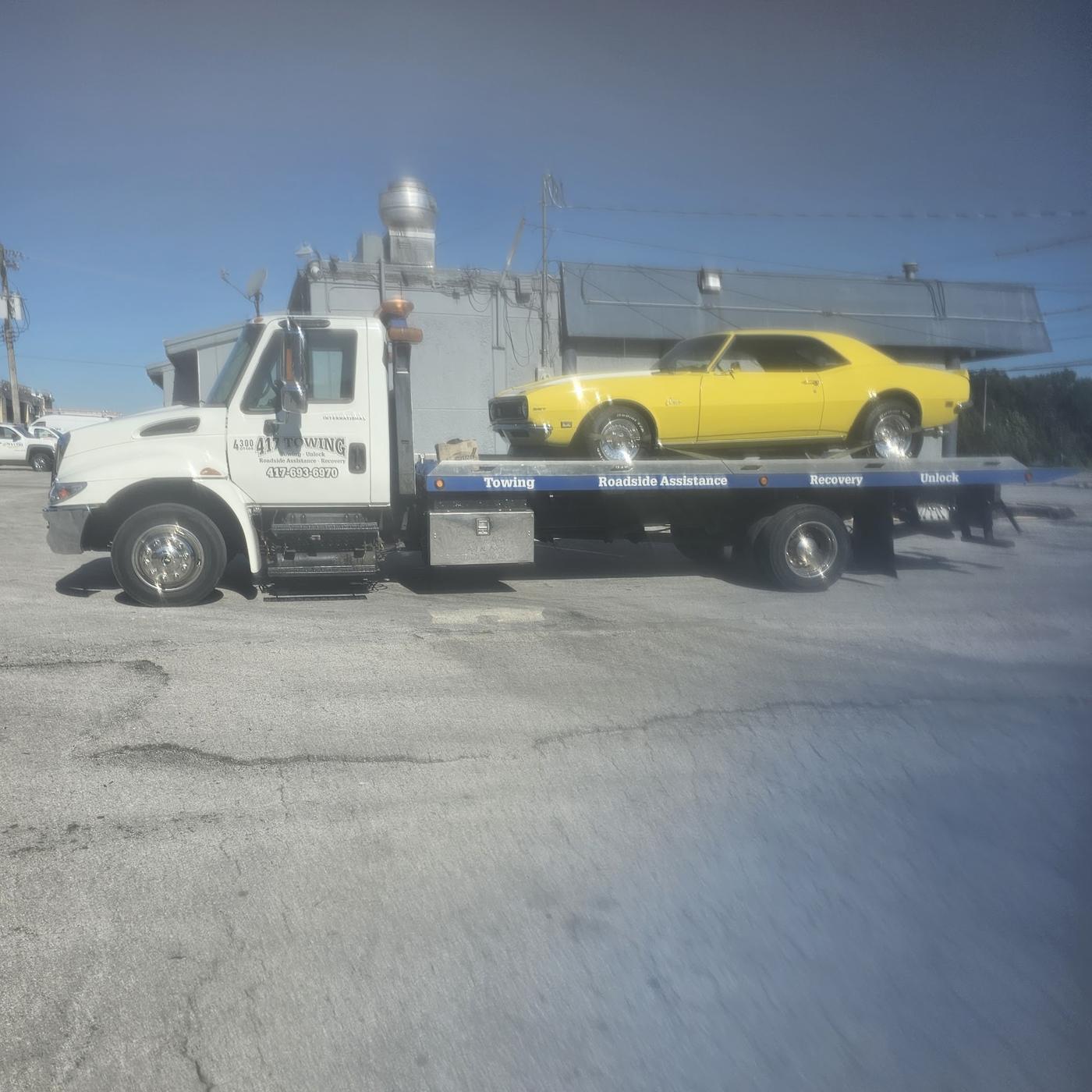 A 417 Towing flatbed with a yellow classic Camaro loaded on the deck